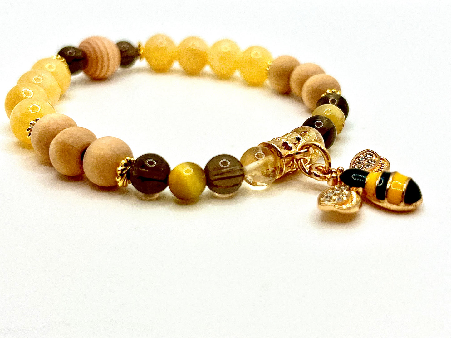 Closeup of Lucky B bracelet featuring yellow, brown and wood beads with gold accents and a gold bee charm