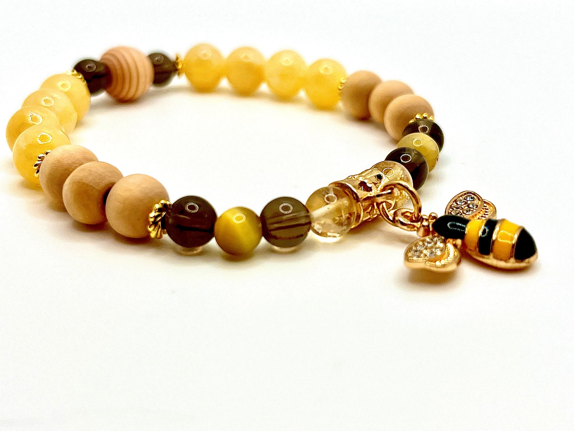 Closeup of Lucky B bracelet featuring yellow, brown and wood beads with gold accents and a gold bee charm