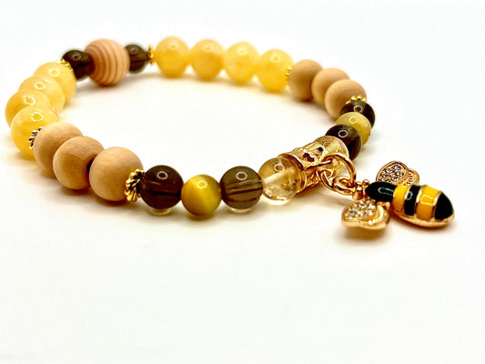 Closeup of Lucky B bracelet featuring yellow, brown and wood beads with gold accents and a gold bee charm